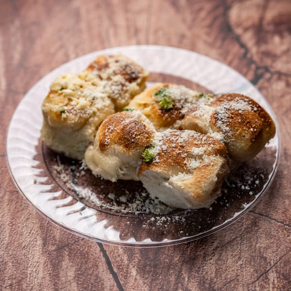 Golden-brown garlic knots dusted with Parmesan cheese and parsley, served on a clear glass plate.