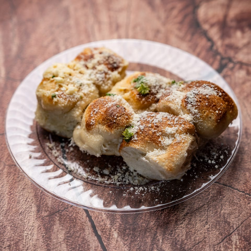 Golden-brown garlic knots dusted with Parmesan cheese and parsley, served on a clear glass plate.