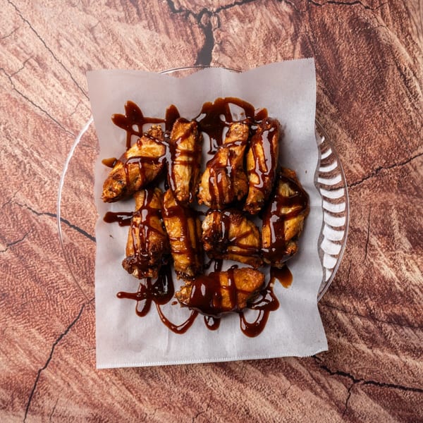 Crispy chicken wings drizzled with a rich, dark BBQ sauce on white parchment paper.