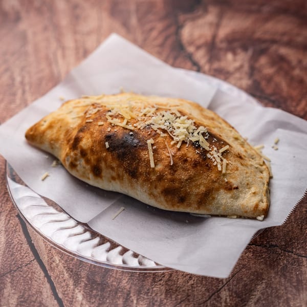 Golden-brown calzone topped with grated cheese, served on white parchment paper on a clear plate.