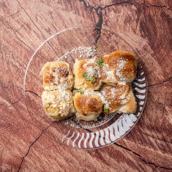Overhead view of golden-brown pierogi dusted with parmesan cheese and parsley on a clear plate.