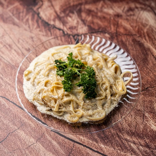 Creamy pasta with black pepper and parsley on a clear plate, on a wooden table.