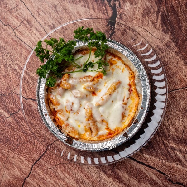 Baked penne pasta with melted cheese and parsley in a foil container on a glass plate.