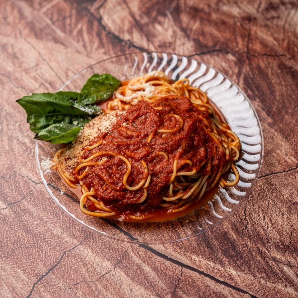 Spaghetti with rich red marinara sauce, grated cheese, and fresh basil on a clear plate.