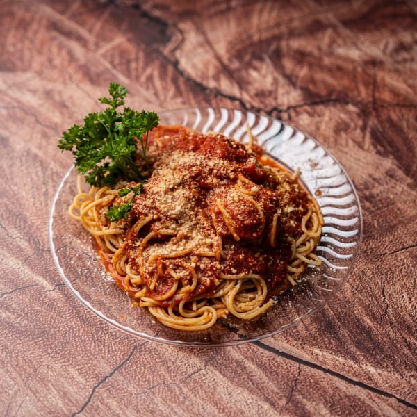 Spaghetti with meatballs, tomato sauce, parmesan cheese, and fresh parsley on a clear plate.
