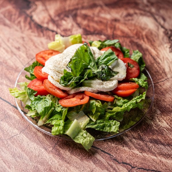 Caprese salad with fresh mozzarella, sliced tomatoes, basil, and lettuce on a clear plate.