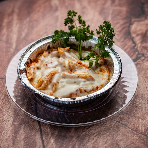 Baked penne pasta with melted cheese and parsley in a foil container on a clear plate.